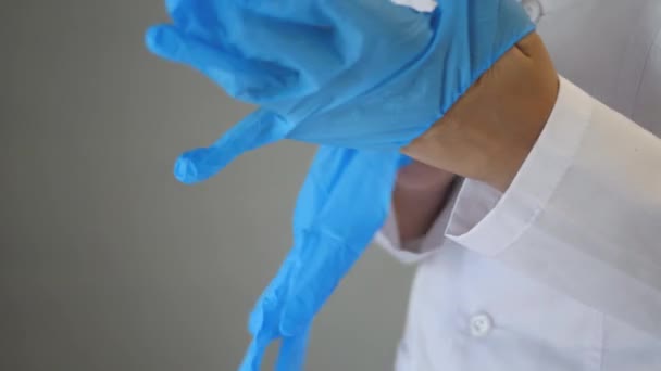 白いコートの医療従事者は、青いゴム滅菌手袋を彼の手に置きます。医者は手術の準備をしている。COVY-19 。閉鎖 — ストック動画