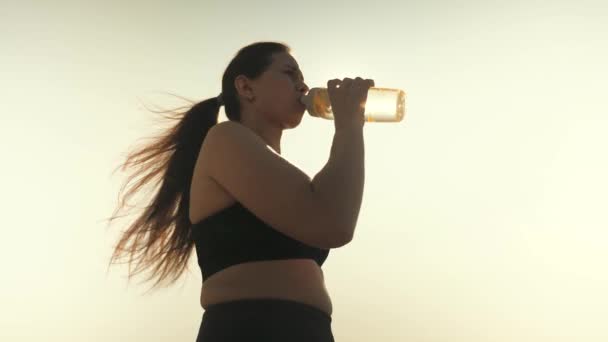 Девушка пьёт воду из бутылки в лучах солнца. Женщина хочет пить после бега. — стоковое видео