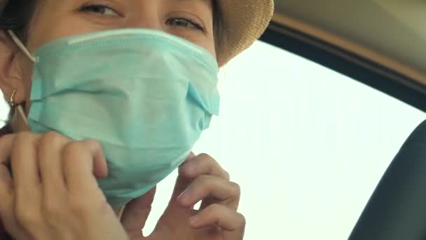 Een jonge vrouw in een auto met een medisch masker om verspreiding van COVID-19 te voorkomen. Rijden vrouw met gezichtsmasker in auto te beschermen tegen het virus griep — Stockvideo