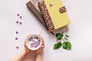 Çocukların ellerinde, bir fincan süt ve leylak çiçekleri. Masaya yayılmış leylak çiçekli kitaplar ve yapraklar..