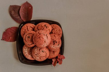 Mavi arka planda renkli sonbahar yaprakları olan siyah bir tabakta kızılcık kurabiyesi. Sonbahar konsepti. Üst görünüm.