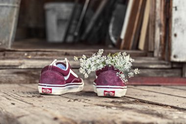Köydeki bir evin ahşap verandasında spor ayakkabıların içinde bir buket yabani çiçek.
