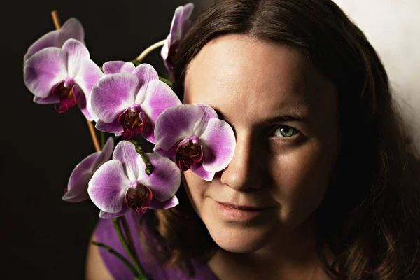 Portrait of a young woman in a purple dress with a blooming orchid. A flower covering one eye.