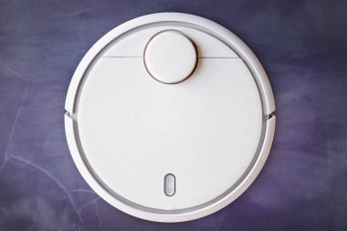 Beyaz bir robot süpürge soyut bir arka planda zemini temizliyor..