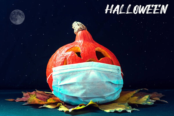Pumpkin in a medical mask with autumn leaves on a dark background. Jack's Lantern. Halloween Decorations 2020. Coronavirus pandemic.