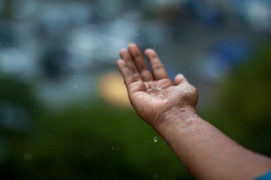 Pencereden yağmur damlalarını yakalayan bir avuç.