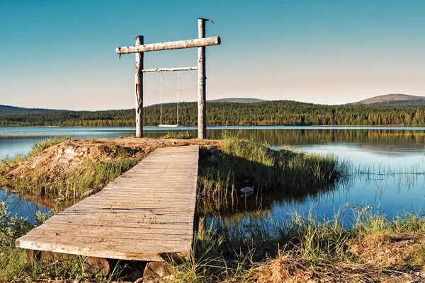 A wooden swing has been set up on a little island in a lake at the Finnish Lapland. The swing is a perfect place to admire the beautiful lake and the nightless night.