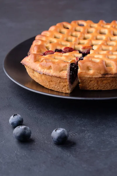 Blueberry pie with a slice cut off and  some berries on black table