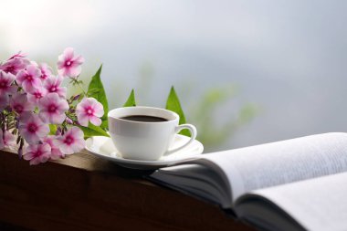 Masada bir fincan kahve, kitap ve çiçekler var.
