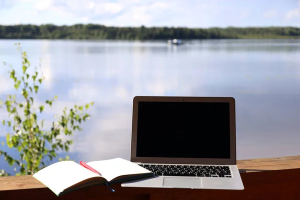 outdoor workplace, laptop and writing on the background of water in a calm environment