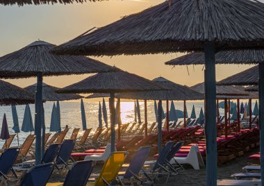 Şemsiyeli gün batımı kumsalı ve turistler olmadan güneşlik yataklar.