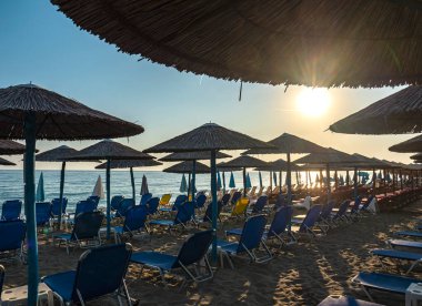 Şemsiyeli gün batımı kumsalı ve turistler olmadan güneşlik yataklar.