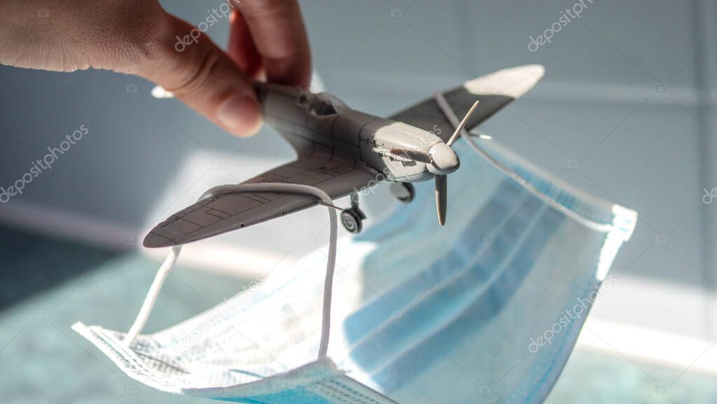 A hand holding a small toy airplane which is carrying a face mask on it's wings