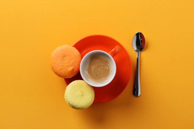 turuncu fincan kahve macaroons üzerinde sarı bir arka plan ile. yukarıdan