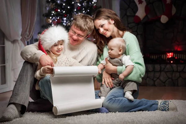 子供を持つ親が読んでサンタ クロースのクリスマス ツリーと暖炉の近くの床の上に座ってのウィッシュ リスト — ストック写真