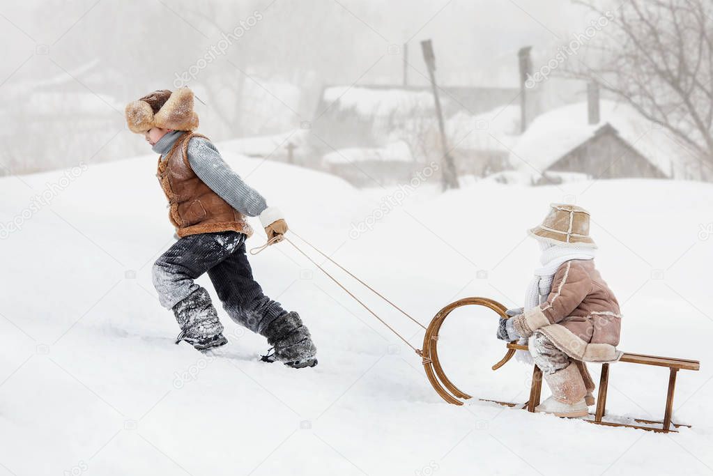 Two children sledding with mountain warm winter day