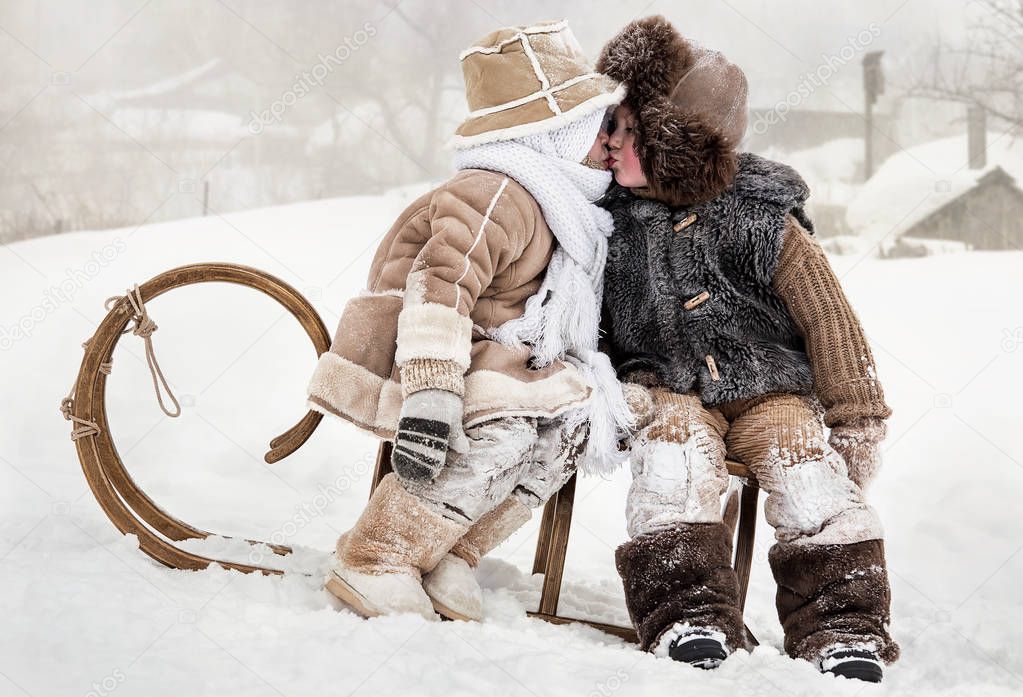 Little boy and girl kissing while sitting on a sled in winter