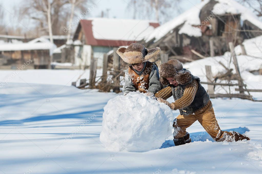 Two little boys sculpt a snowman in the backyard of the house clear winter day
