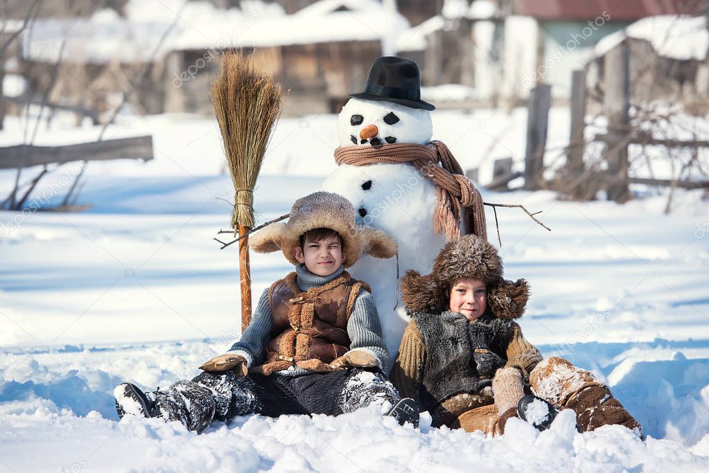 Two little boys sculpt a snowman in the backyard of the house clear winter day