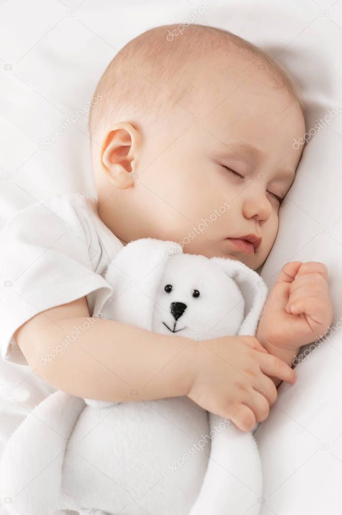 Carefree sleep little baby with a soft toy on the bed