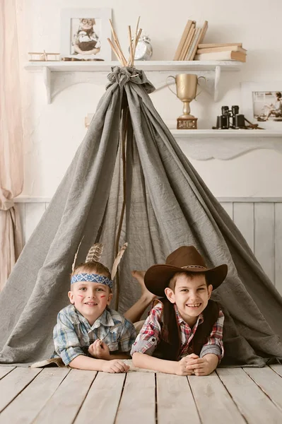 Мальчики, как индеец и ковбой играют в ее комнате — стоковое фото