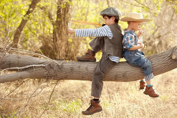 Los chicos soplan burbujas y disparan con la honda, sentados en un árbol — Foto de Stock