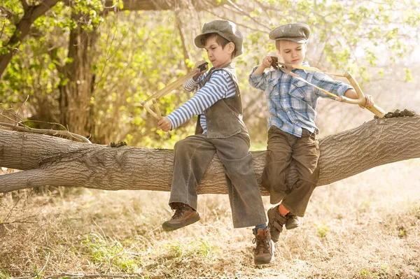 Chłopcy z proce siedzi na gałęzi drzewa — Zdjęcie stockowe