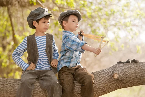 Boys with slingshots sitting on a tree branch — Stock Photo, Image