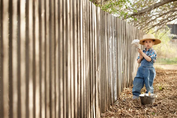 Мальчик красит старый забор — стоковое фото