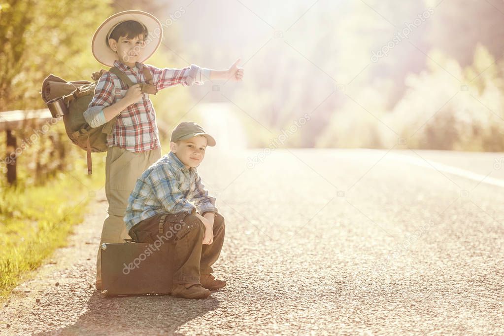 Boys travelers on a mountain road with a backpack and a suitcase