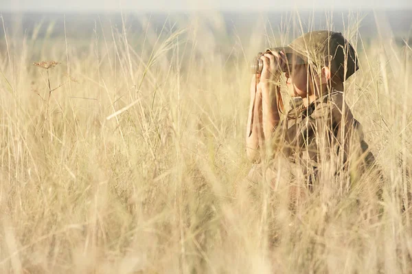 Chłopiec patrząc przez lornetkę w gęstej suchej trawie — Zdjęcie stockowe