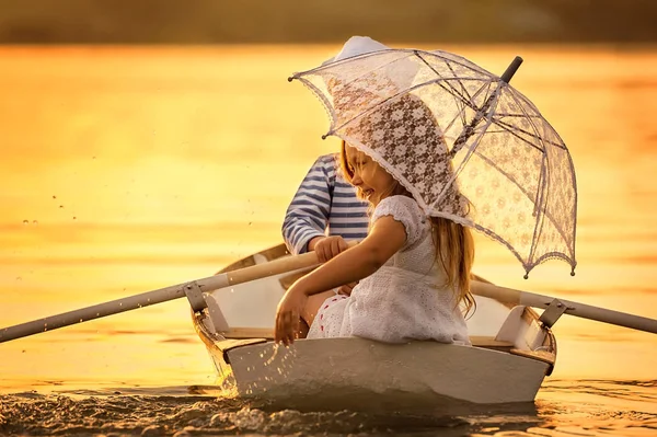 Niño con una chica flotando en un bote remando a través del lago —  Fotos de Stock