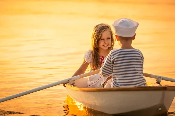 Niño con una chica flotando en un bote remando a través del lago —  Fotos de Stock