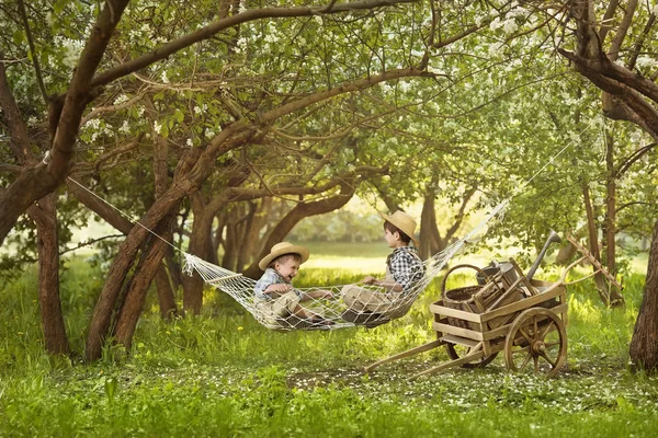 Unge gartnere hviler i en hængekøje under træerne efter arbejde - Stock-foto