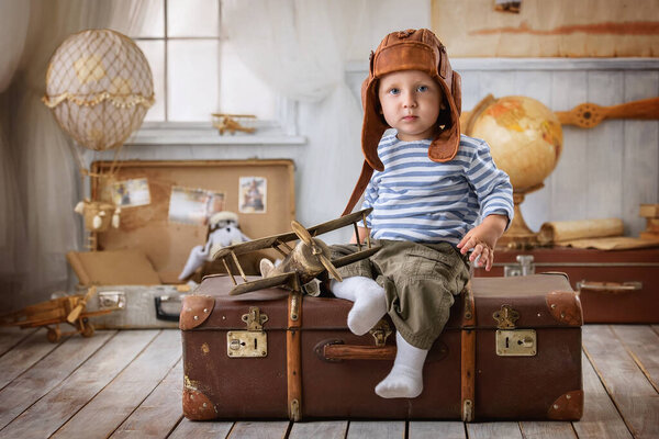 Little boy is himself an aviator and plays with the airplane sitting on a suitcase