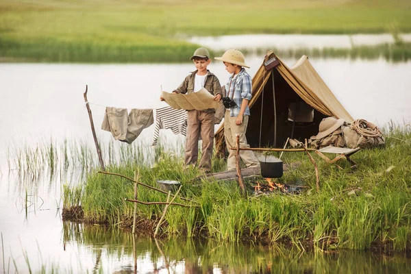 Two boys set up camp, and kindle the fire, sitting on the shore of the lake on a summer evening