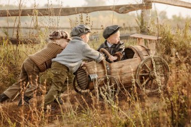 Kırsal bir sonbahar akşamında, tahta varillerden üçüncü yarış arabasına binen iki genç çocuk.