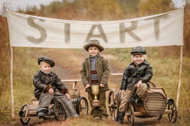Üç küçük oğlan yarışçı, sonbahar yağmurlu günlerinde arka planda doğaçlama ahşap arabalarda yarışıyor. Retro için rötuş