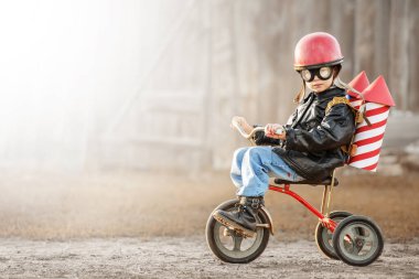 Evin arka bahçesinde oynayan binici ve roketçi görünümünde bir çocuk.