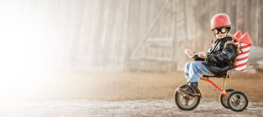 Evin arka bahçesinde oynayan binici ve roketçi görünümünde bir çocuk.