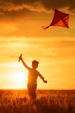 Çocuk gün batımında bir uçurtma fırlatıyor.