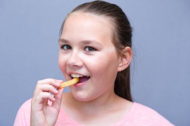 Kız bir bankta oturur ve açık ağzı ile patates yiyor