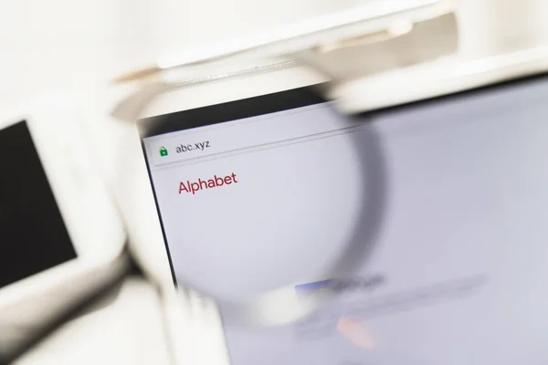 Los Angeles, California, USA - 27 February 2019: Alphabet Inc. official website homepage under magnifying glass. Concept Alphabet Inc. logo visible on smartphone, tablet screen, — Stock Photo, Image