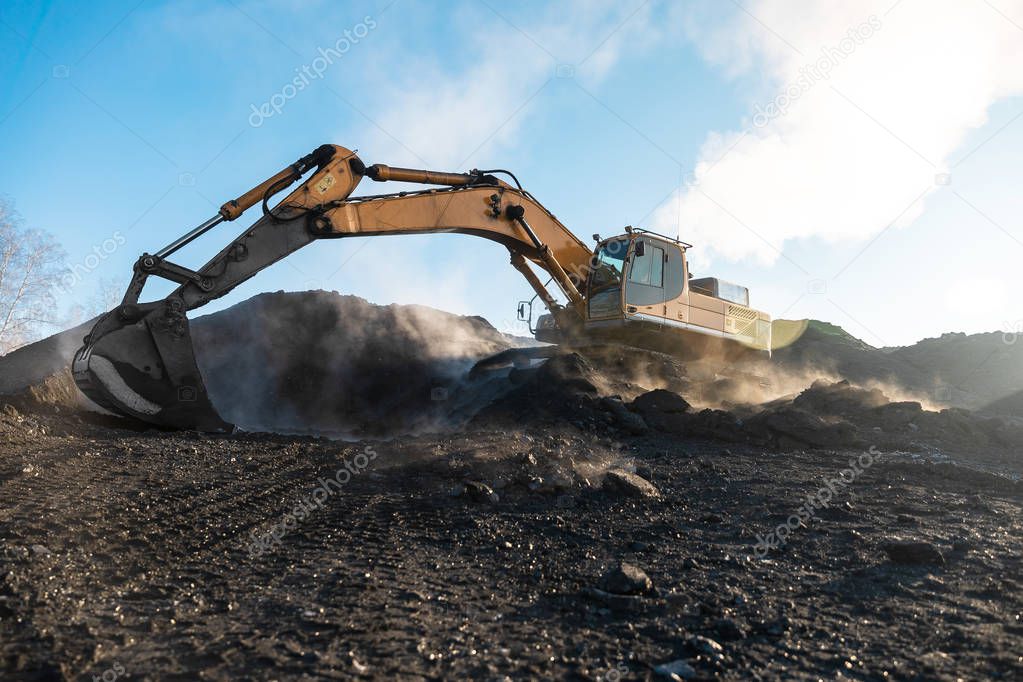 Yellow big excavator in the coal mine, loads the breed, with the bright sun and nice blue sky in the background. Mining truck mining machinery. Technique in coal mine