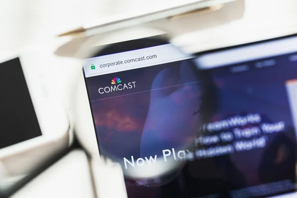 New York, SUA - 4 martie 2019: Pagina principală a Comcast Corporation sub lupă. Logo-ul Comcast Corporation vizibil pe smartphone, ecran tabletă — Fotografie, imagine de stoc