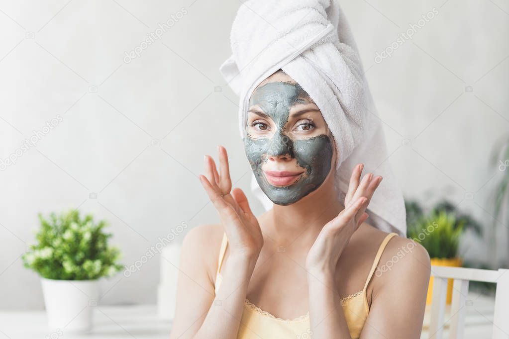 Face Skin care. Attractive Young Woman Wrapped in Bath Towel, applying clay mud mask to face. Skin care concept. Girl taking care of complexion. Beauty treatments