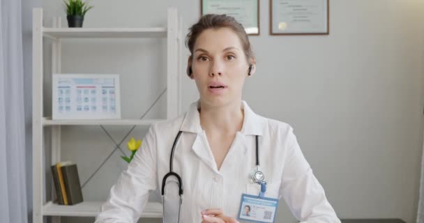 医生使用虚拟聊天电脑应用与病人交谈。女医生穿着医疗服，带着耳机，用手提电脑给远方的病人打电话。远程医疗远程保健服务概念 — 图库视频影像