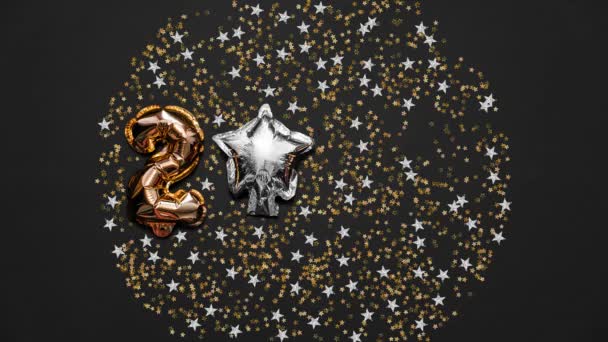 Top view, stop motion shot christmas, holidays and celebration concept balloons in the form of numbers 2021 with confetti on black background. Colorful alternate Christmas and New Year holidays Stock Video