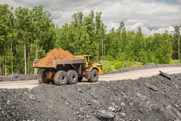 Large quarry dump truck. Big yellow mining truck at work site. Loading coal into body truck. Production useful minerals. Mining truck mining machinery to transport coal from open-pit production