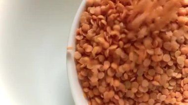 Kırmızı mercimek ya da mazoor dal, izole edilmiş beyaz kase üzerine dökülüyor.